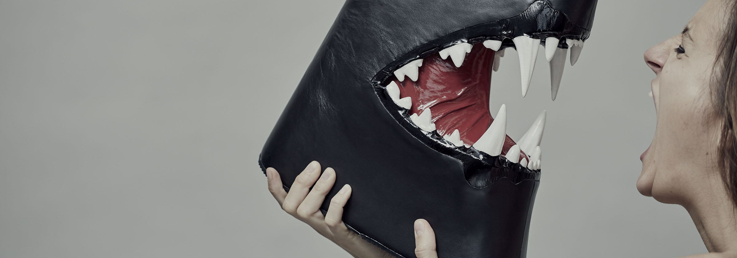 Black boot with sharp teeth held by female model screaming at it