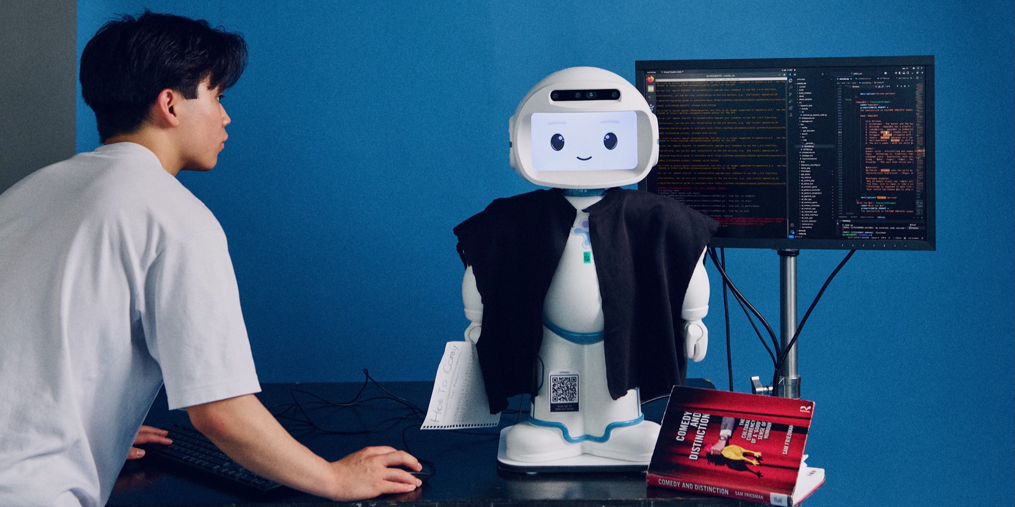 A student developing code for his Comedy Robot, with code on screen, against a striking blue background