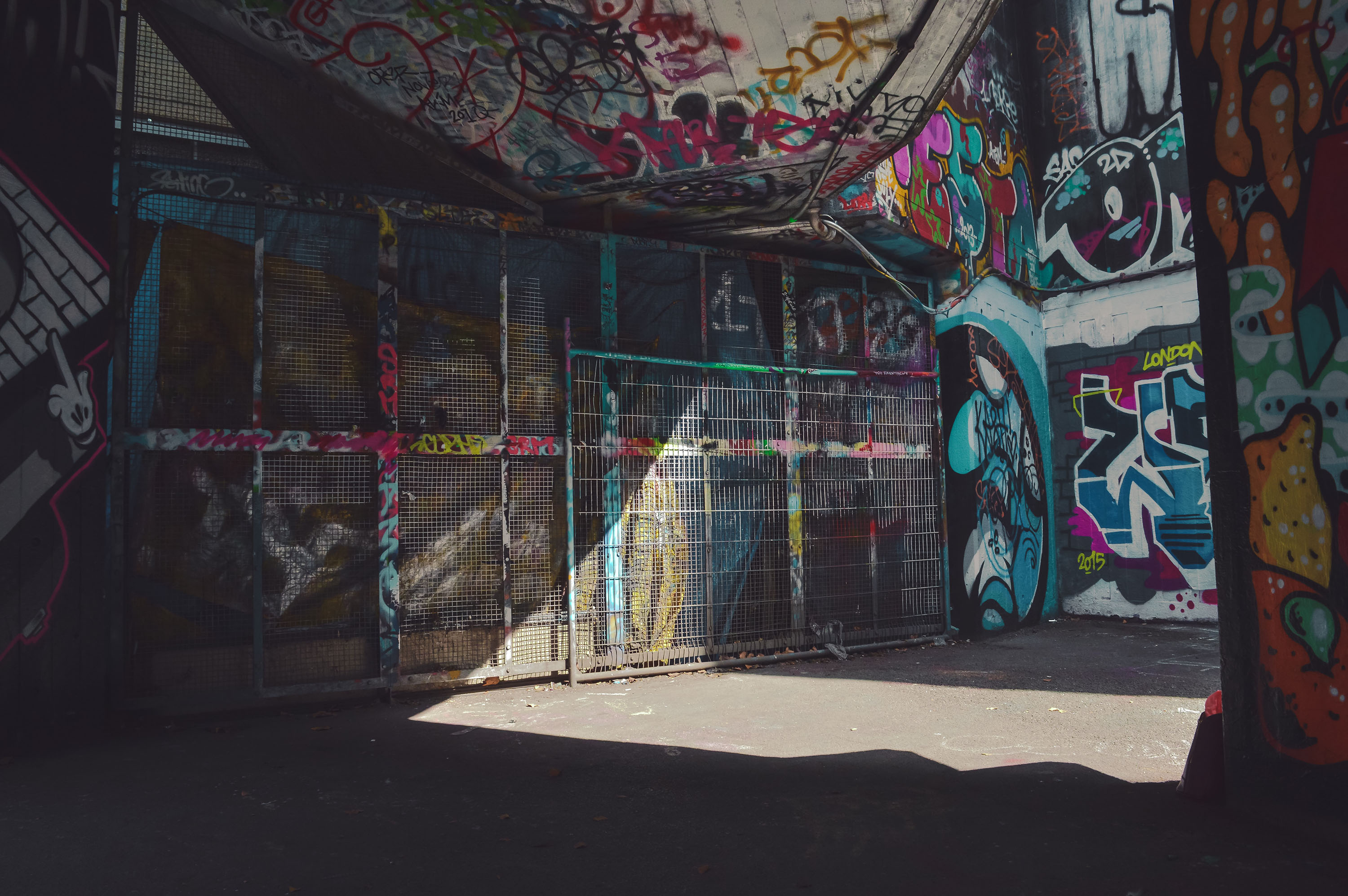 A wall is covered in graffiti in tones of black, blue and pink