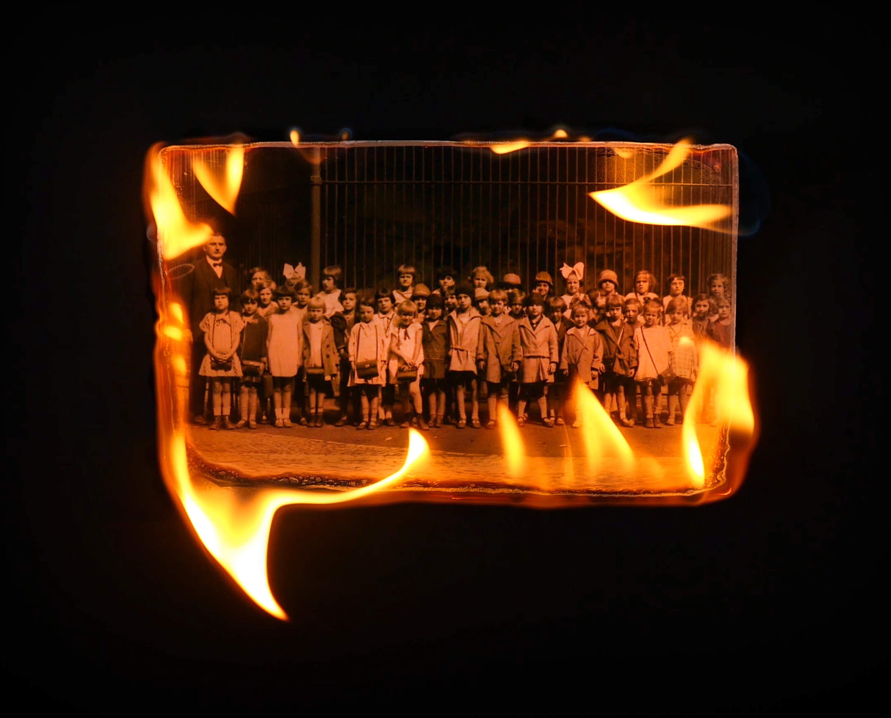 Video still of film For Leopold, featuring a photograph of children, its edges burning.