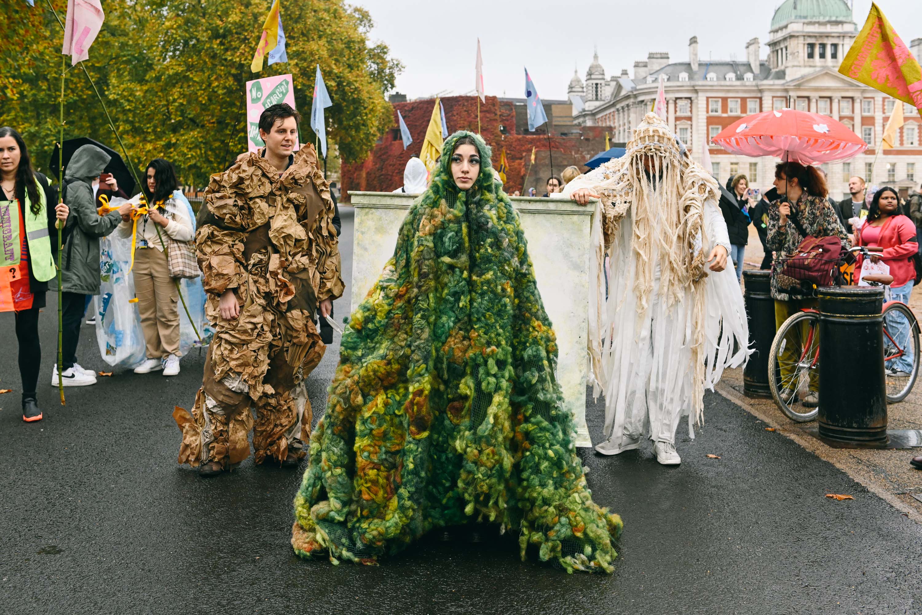 Figures standing  wearing green moss, cardboard and pale fabric garments