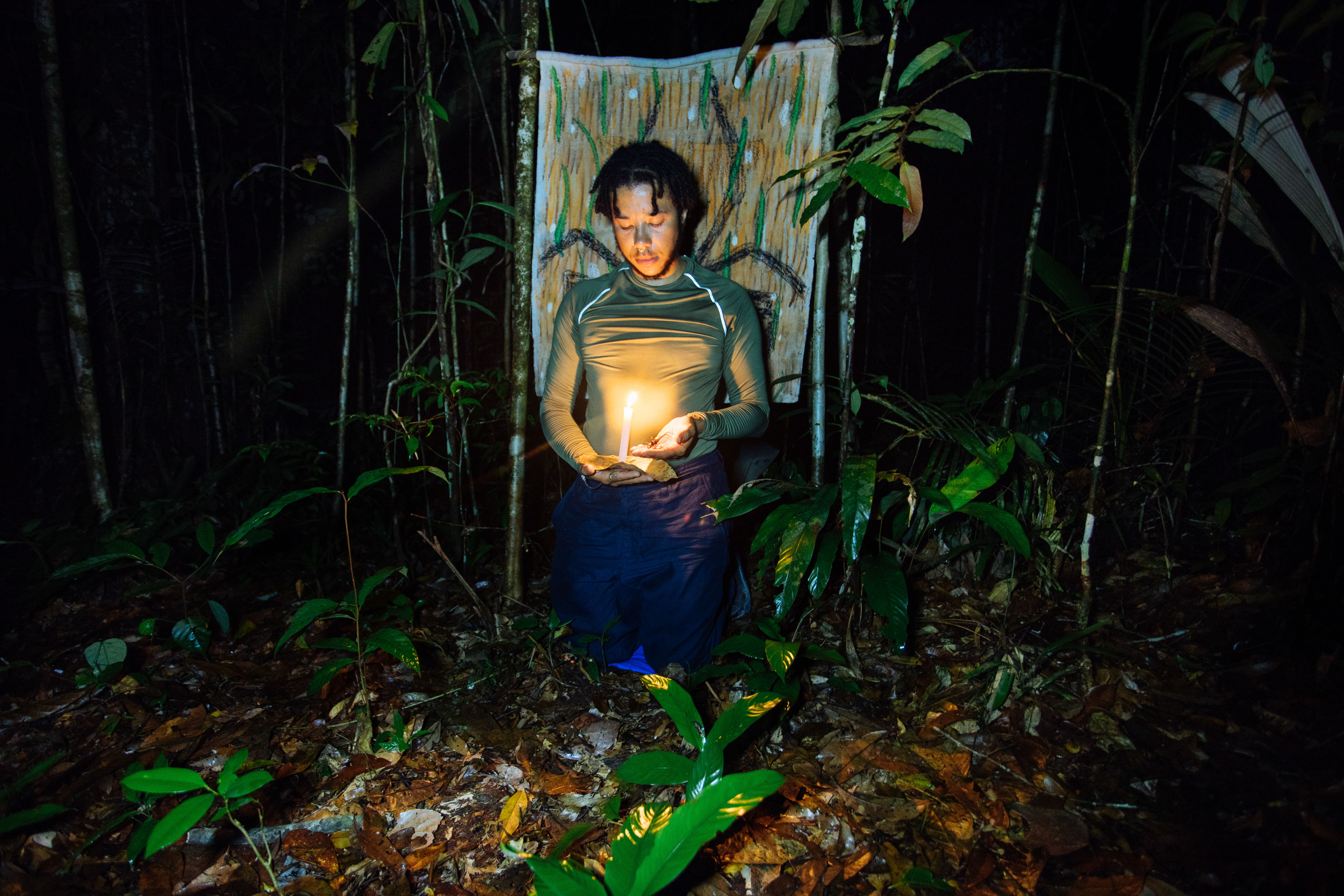 Photograph of Rudy Loewe in Amazonia at night with a candle, talking with an arachnid. 