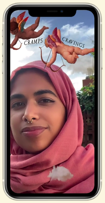 Smiling woman in a salmon coloured headscarf against a blue sky and clouds, with 2 illustrated cherubs above her head and the words 'Cramps' and 'Cravings'