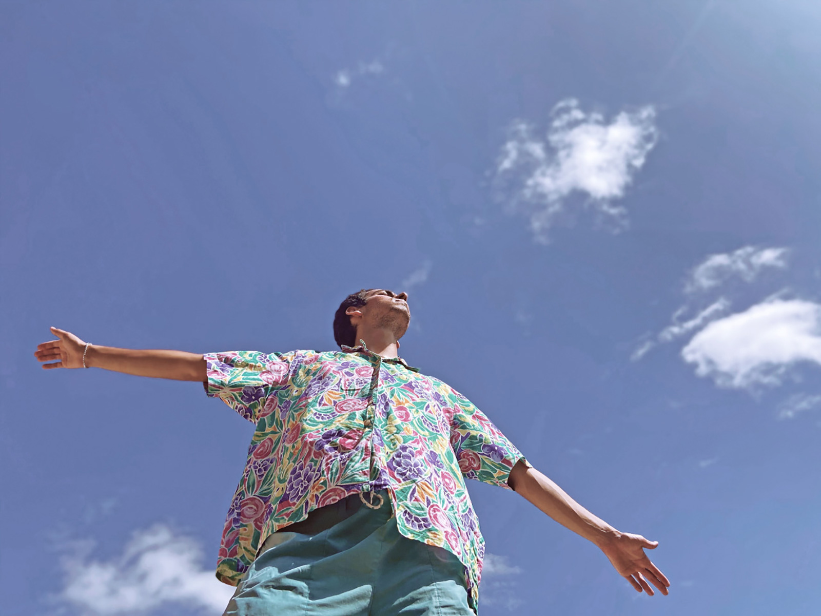 A photograph of a man raising his arms to a blue sky.