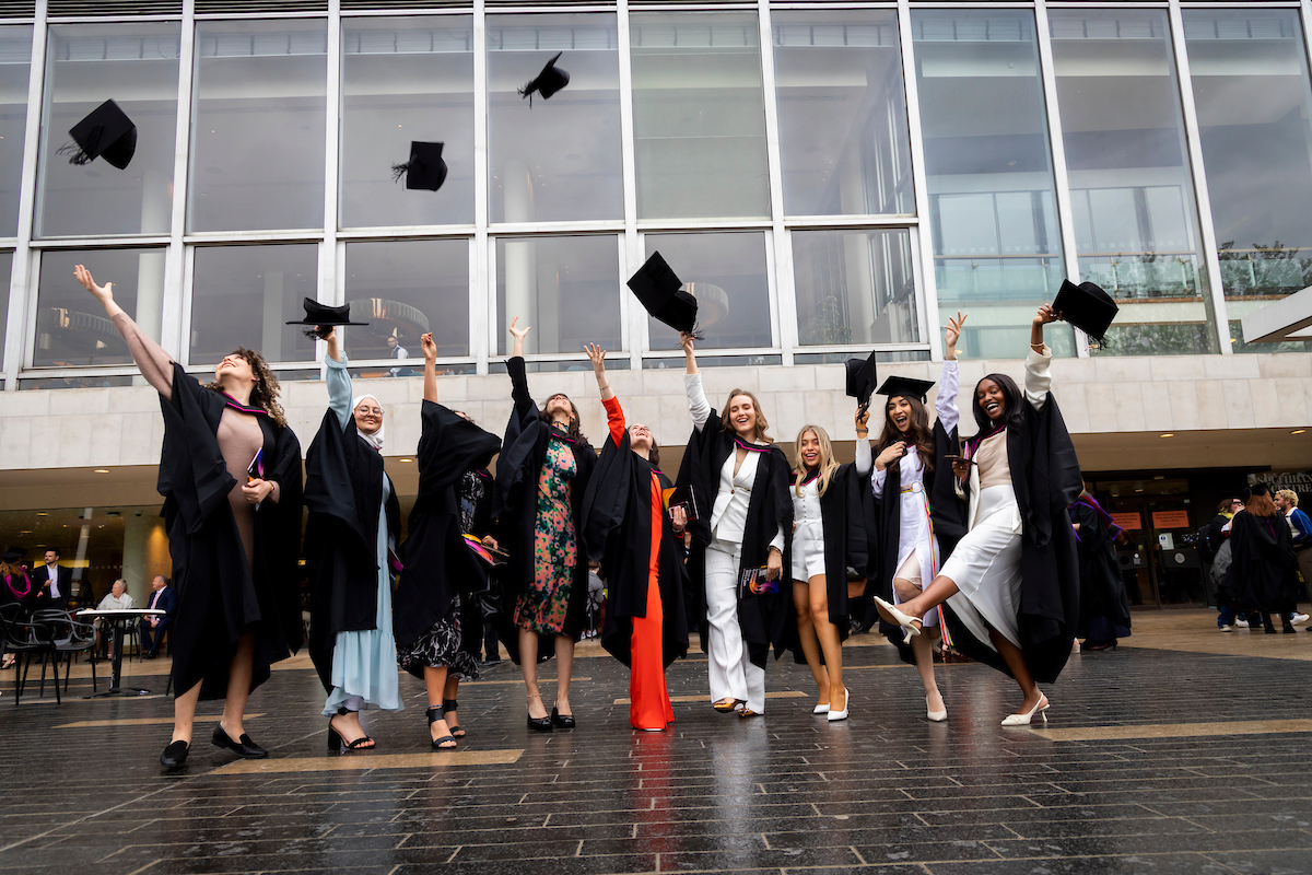 people wearing academic gowns, throwing mortarboards into air in celebration