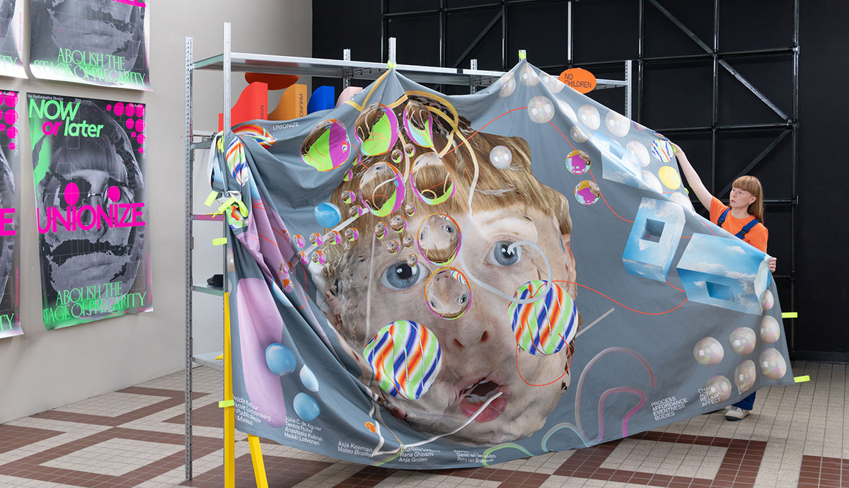An artist stands beside a bedsheet-sized artwork depicting a face surrounded by coloured bubbles.