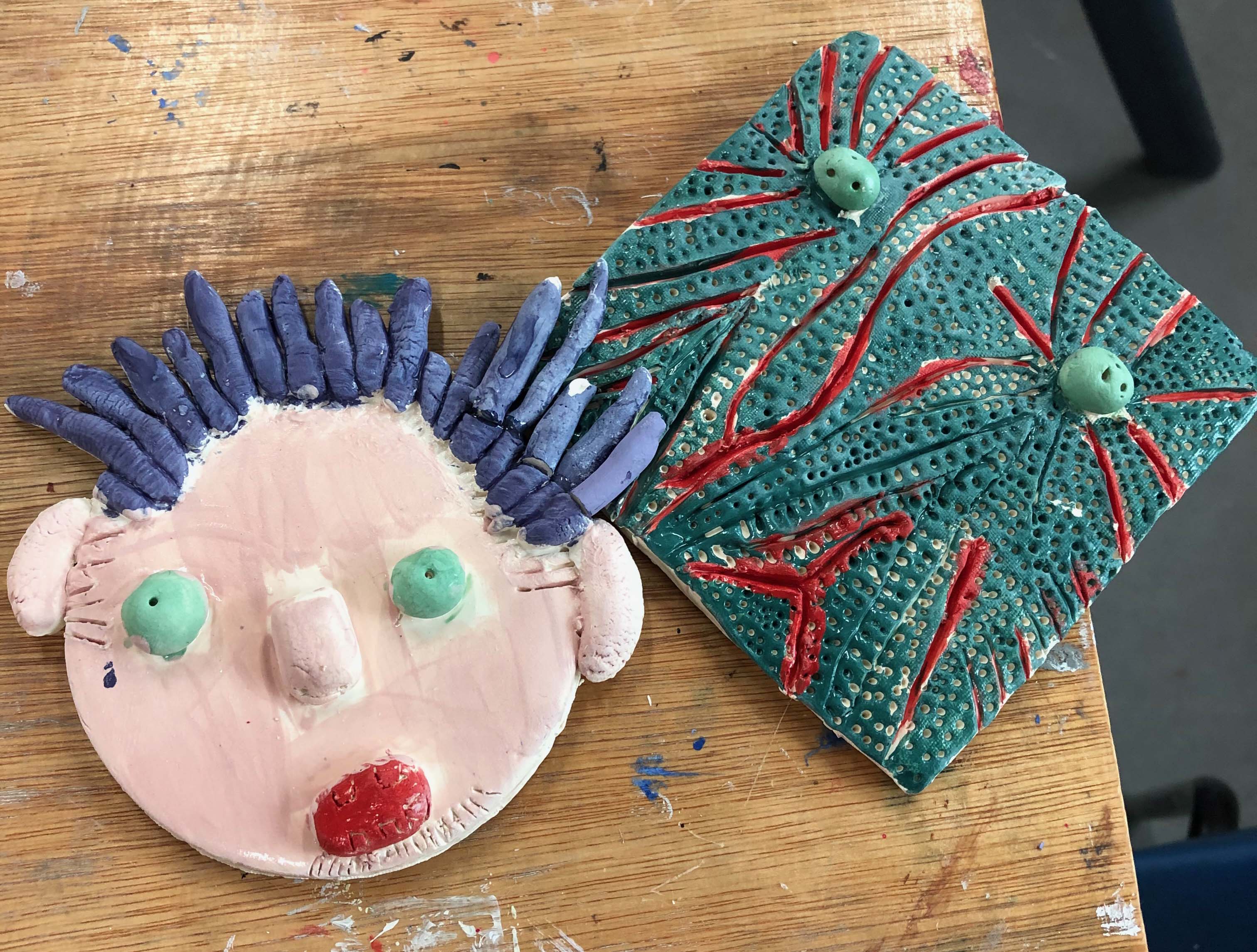 two clay tiles, the left shows a face with blue hair, the right is abstract turquoise and red pattern 