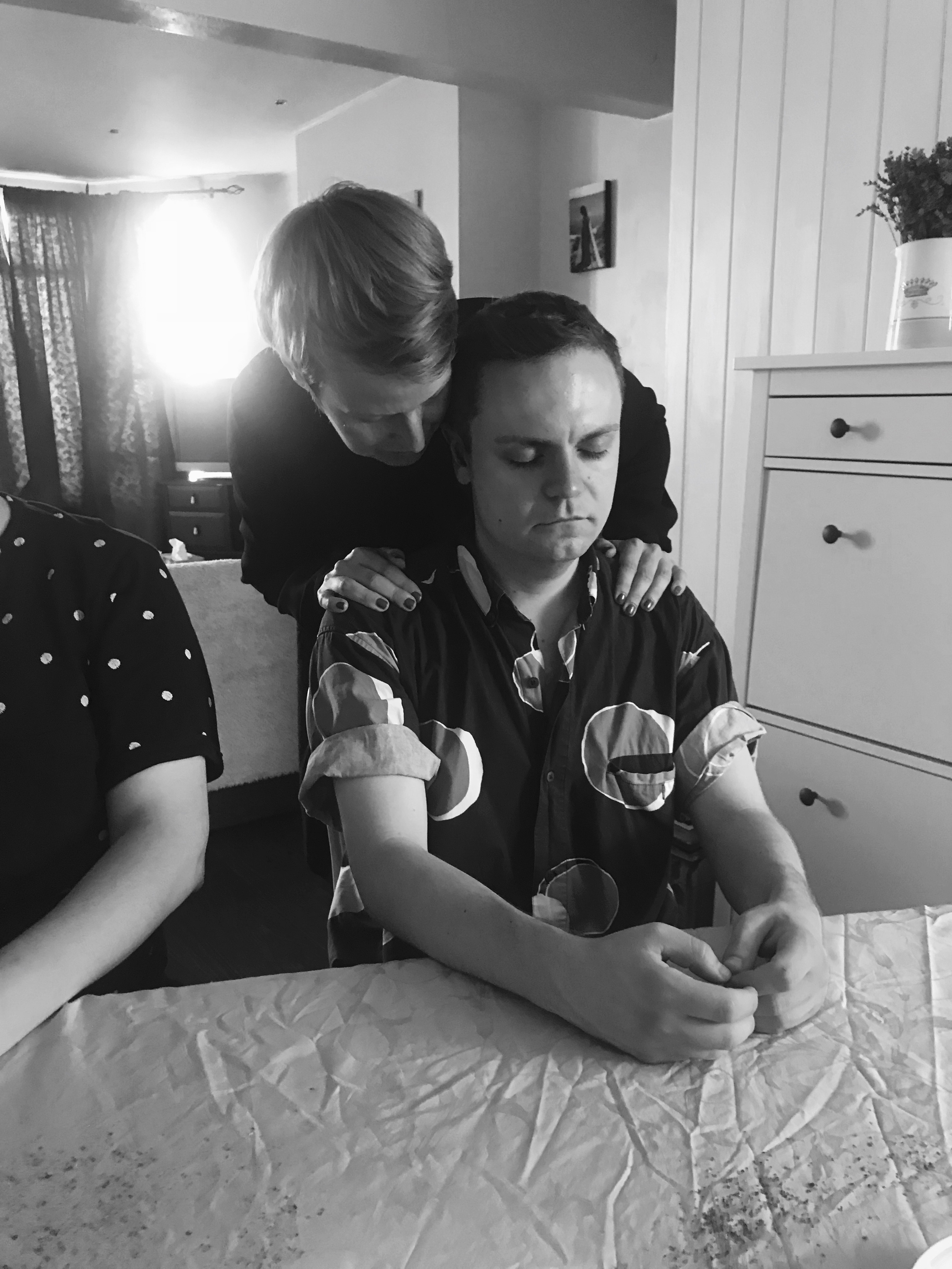 a black and white photo of a woman whispering into a man's ear standing behind him