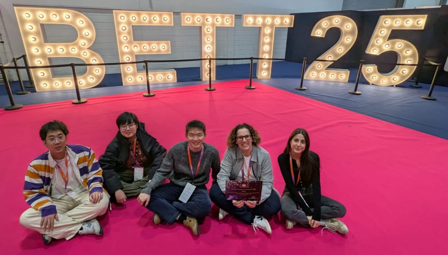 Five students sat on a pink carpet in front of lit up letters.