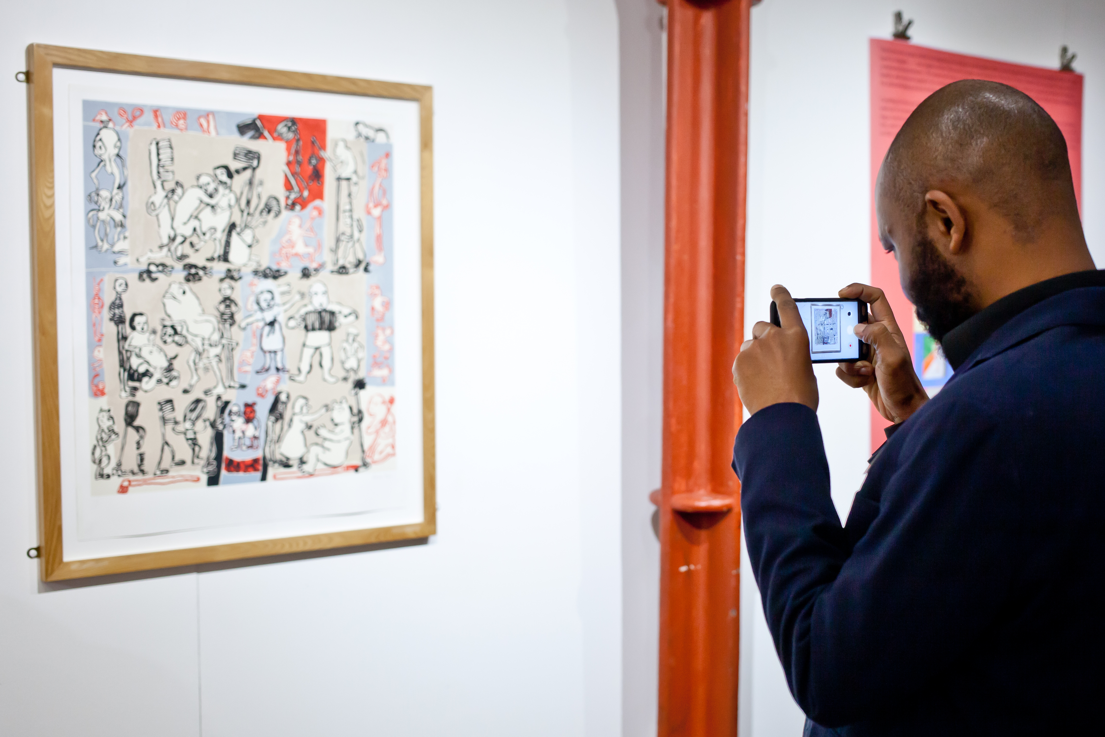A man taking a photo of a piece of art hung on a wall