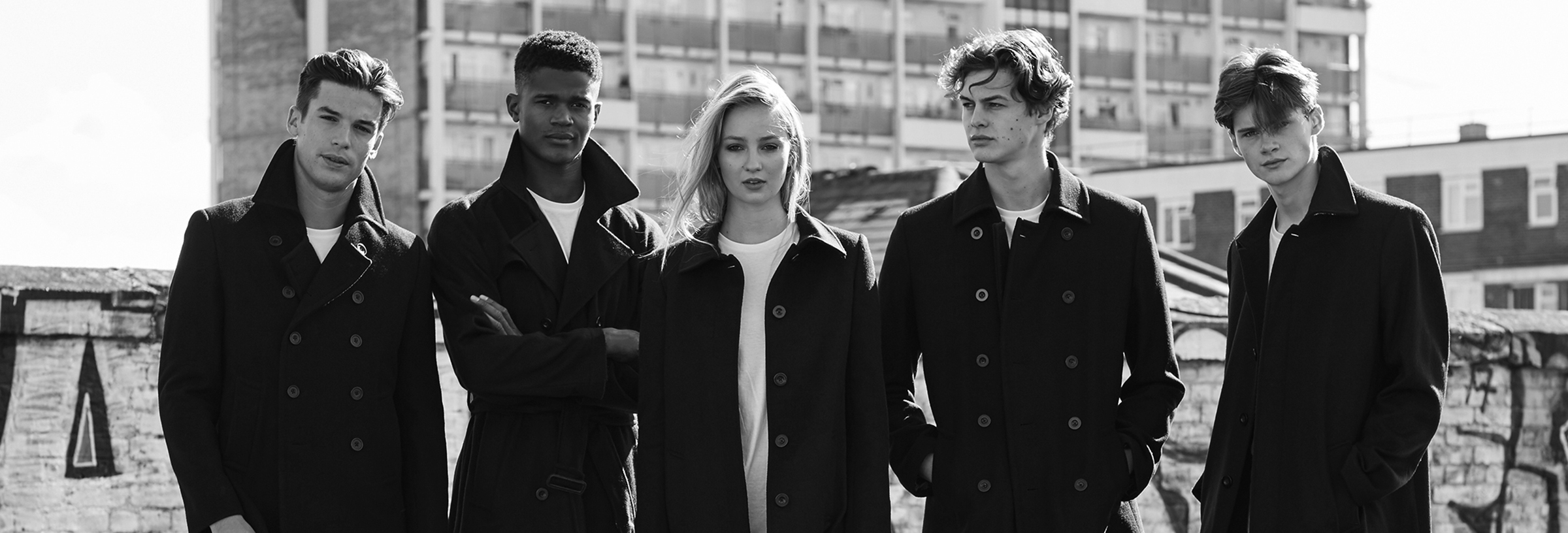 4 male models and 1 female model wearing black and white rustic clothing standing at a block of deserted flats