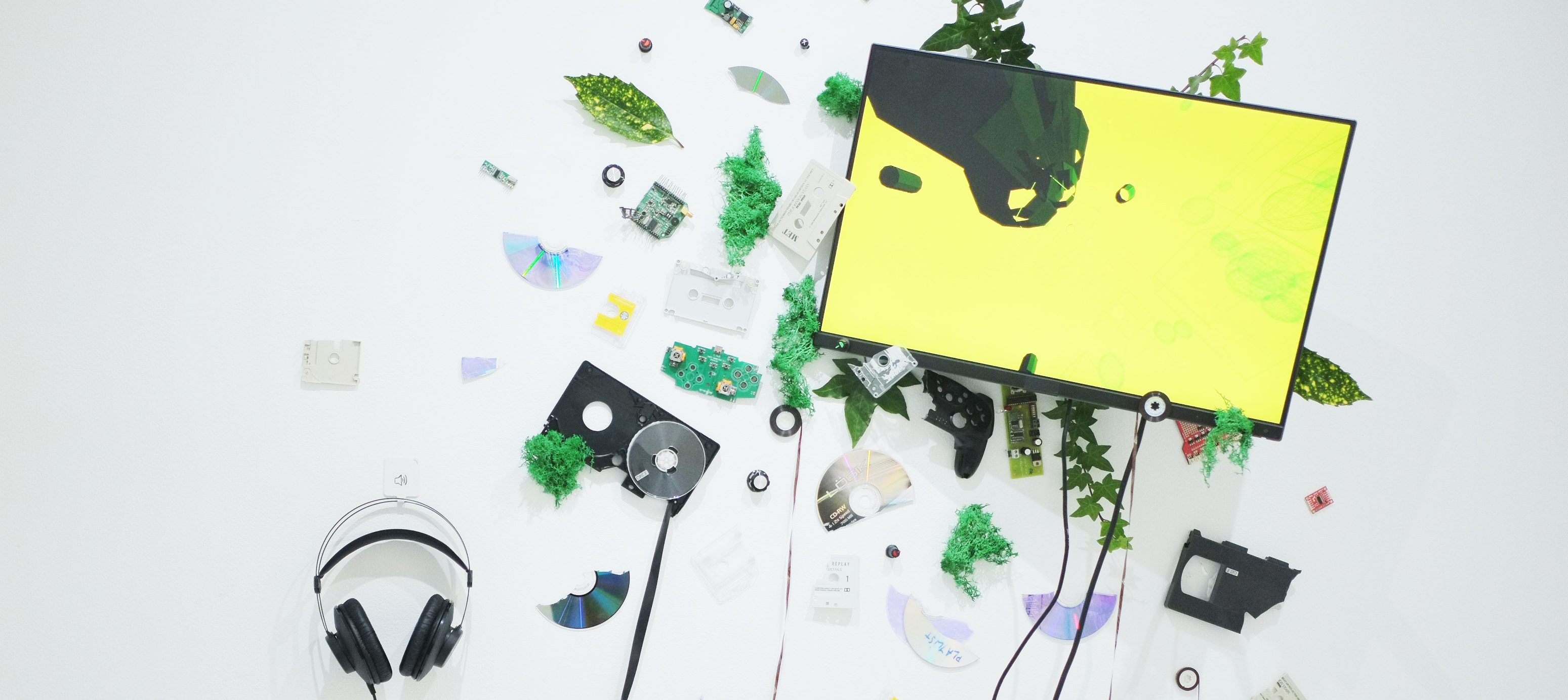 White wall with a screen surrounded by a series of objects, including a pair of headphones.