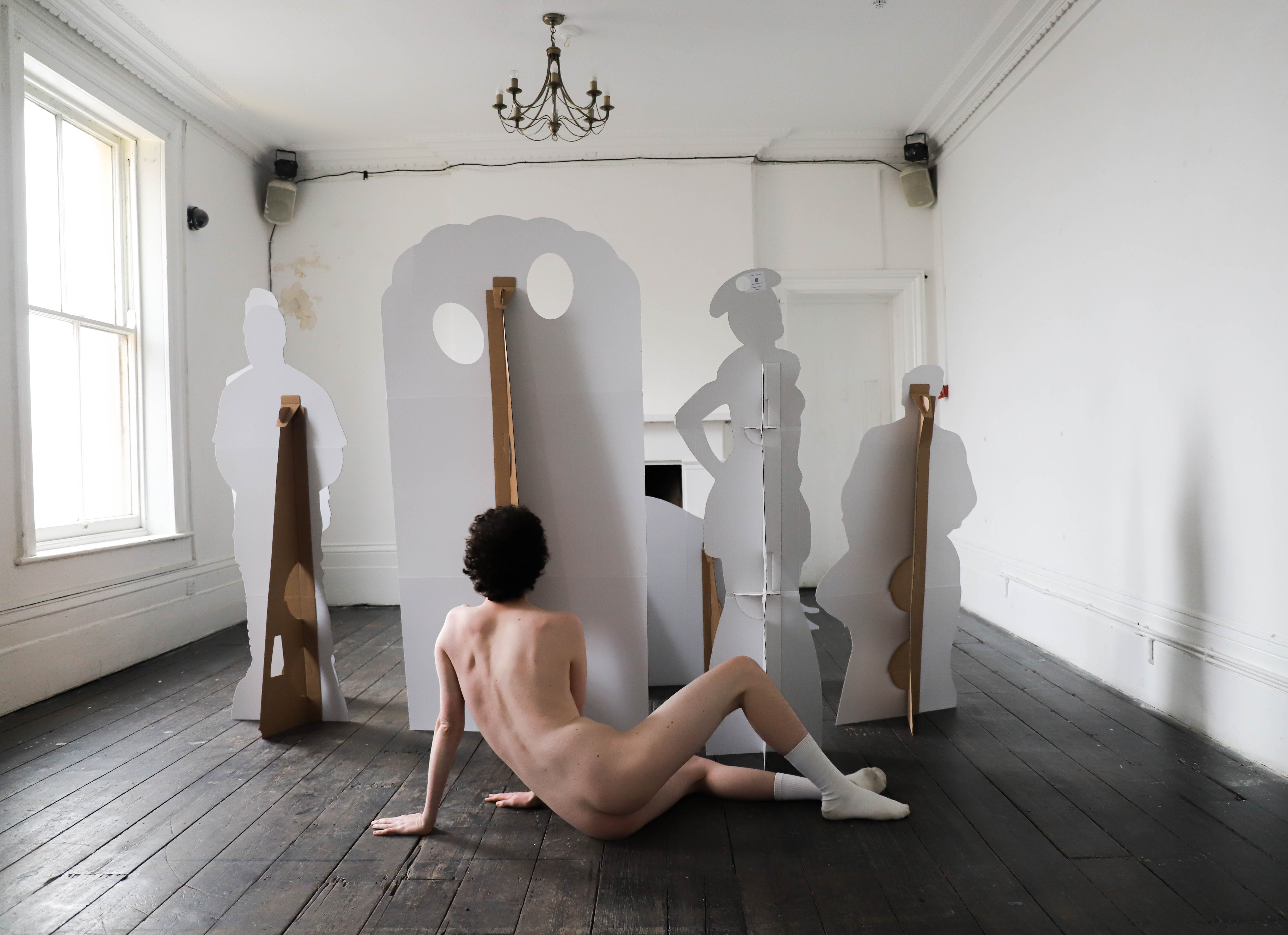 A person wearing only socks lying on their side behind some cardboard cutouts