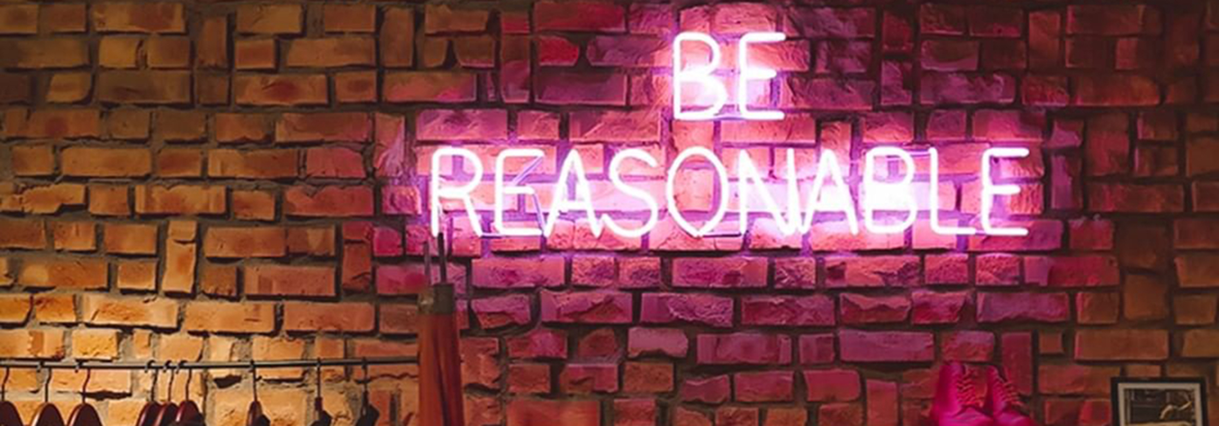 Be reasonable written in pink illuminous lights against a brick wall