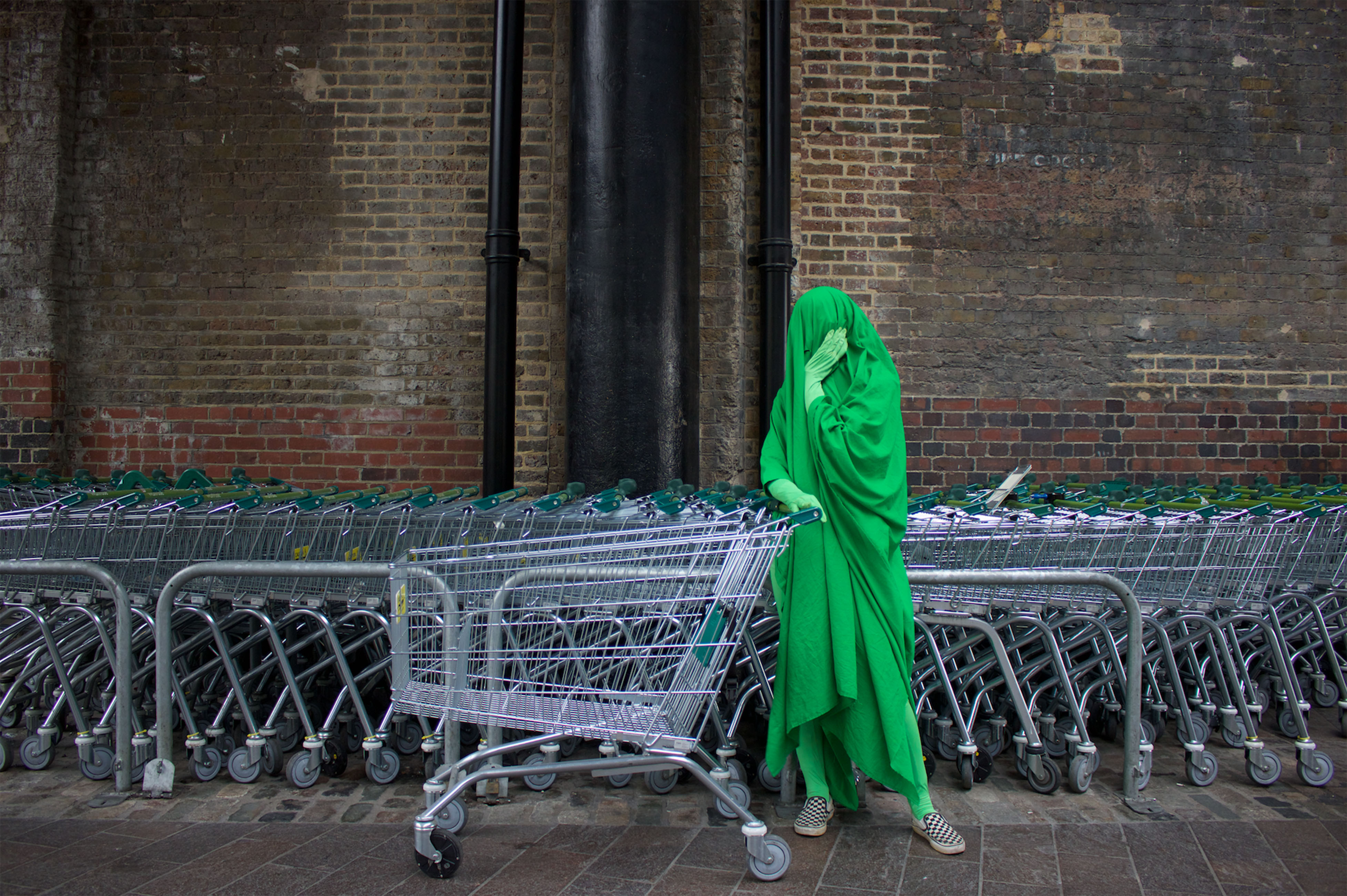 Person covered in green pushing shopping trolley