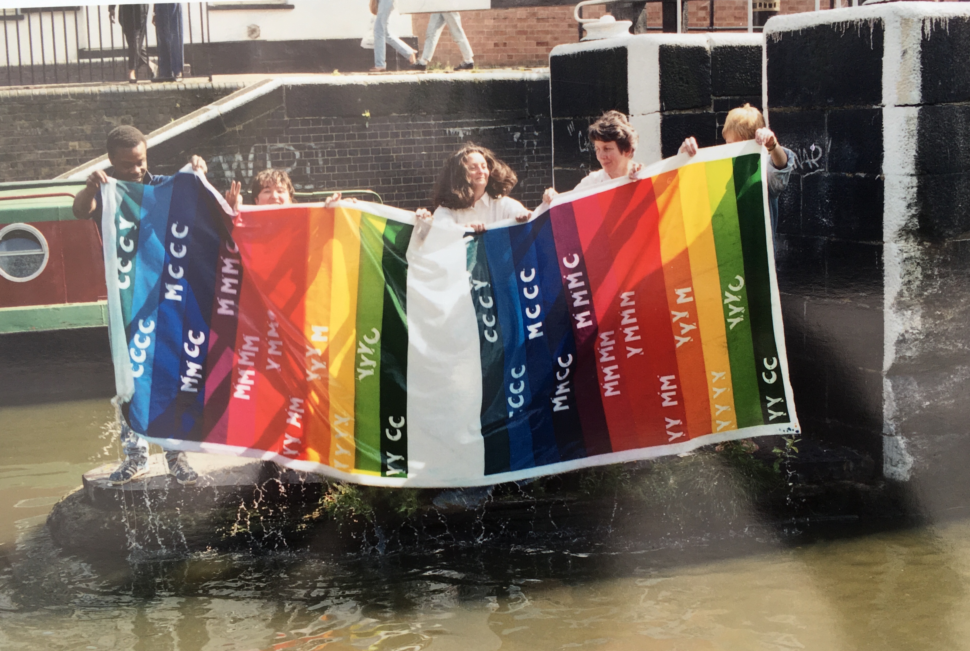 A group of 5 people holding up a colourful printed piece of fabric