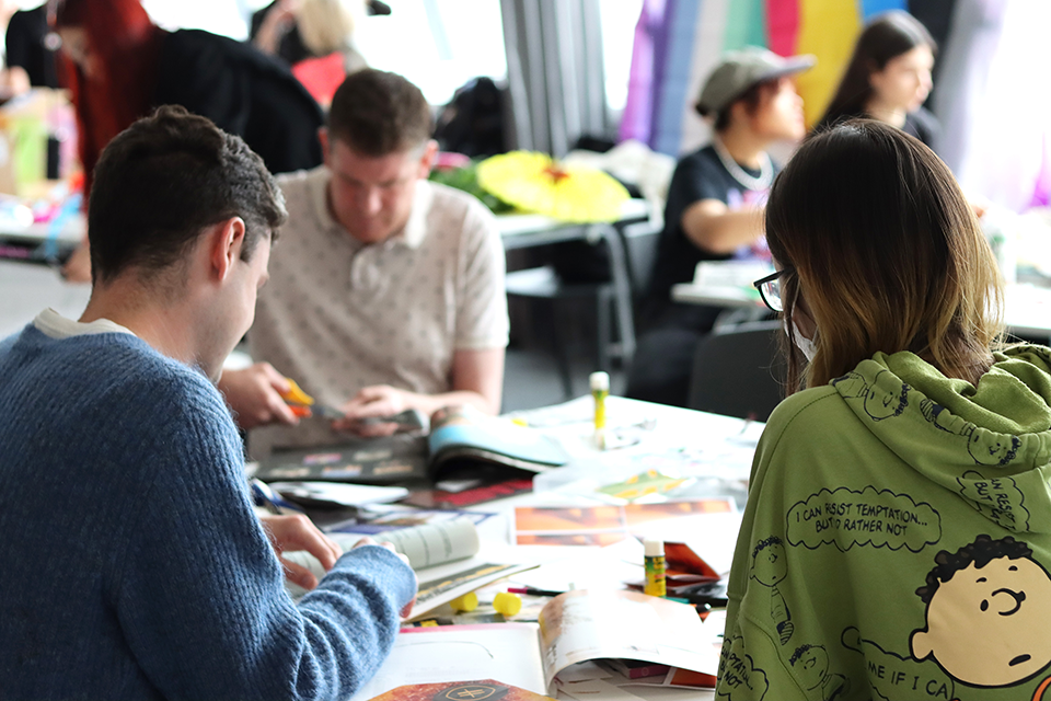 People sat around a table making zines with their backs facing the camera