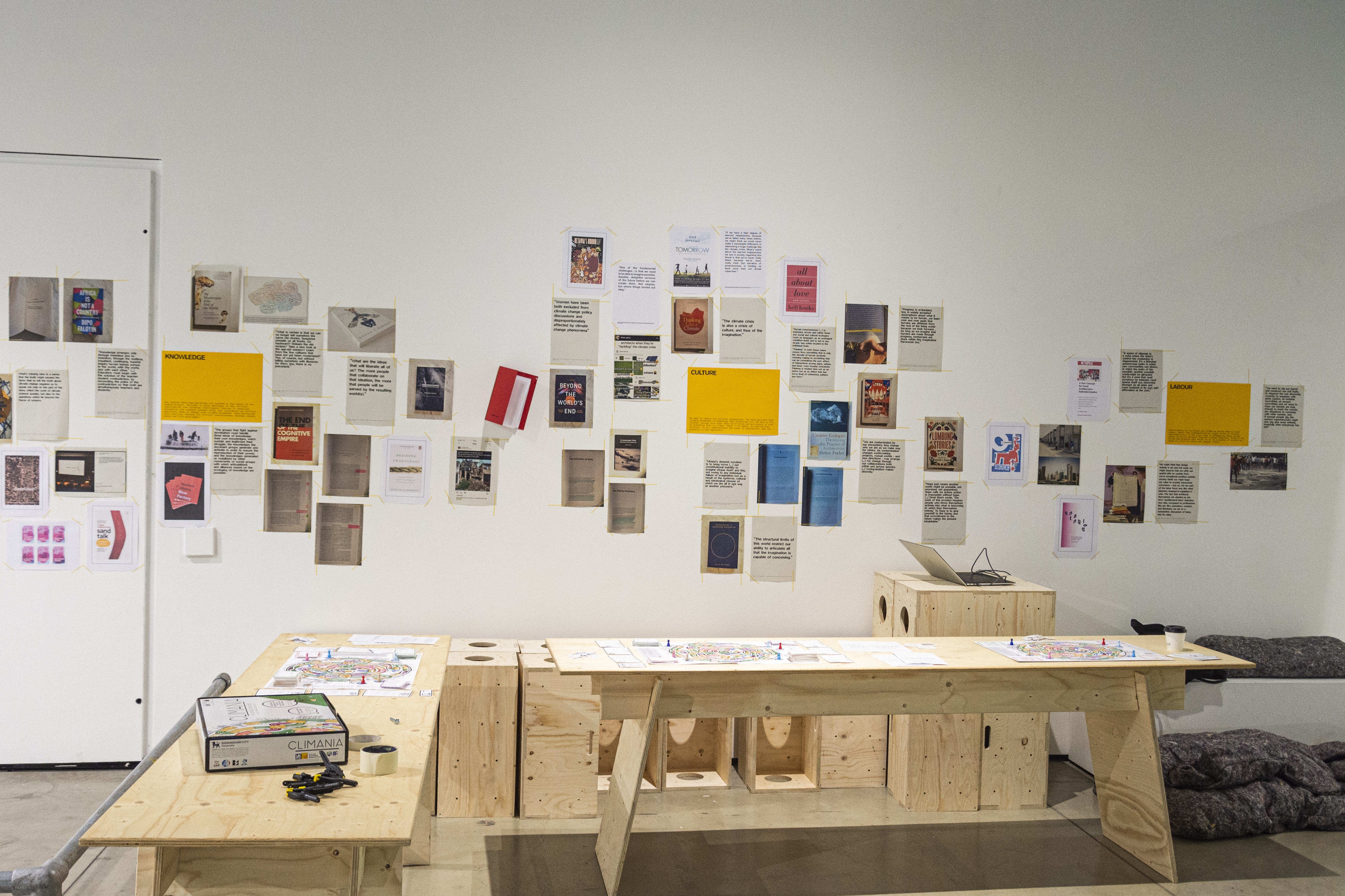An exhibition space with lots of colourful posters hanging on the wall next to a wooden bench