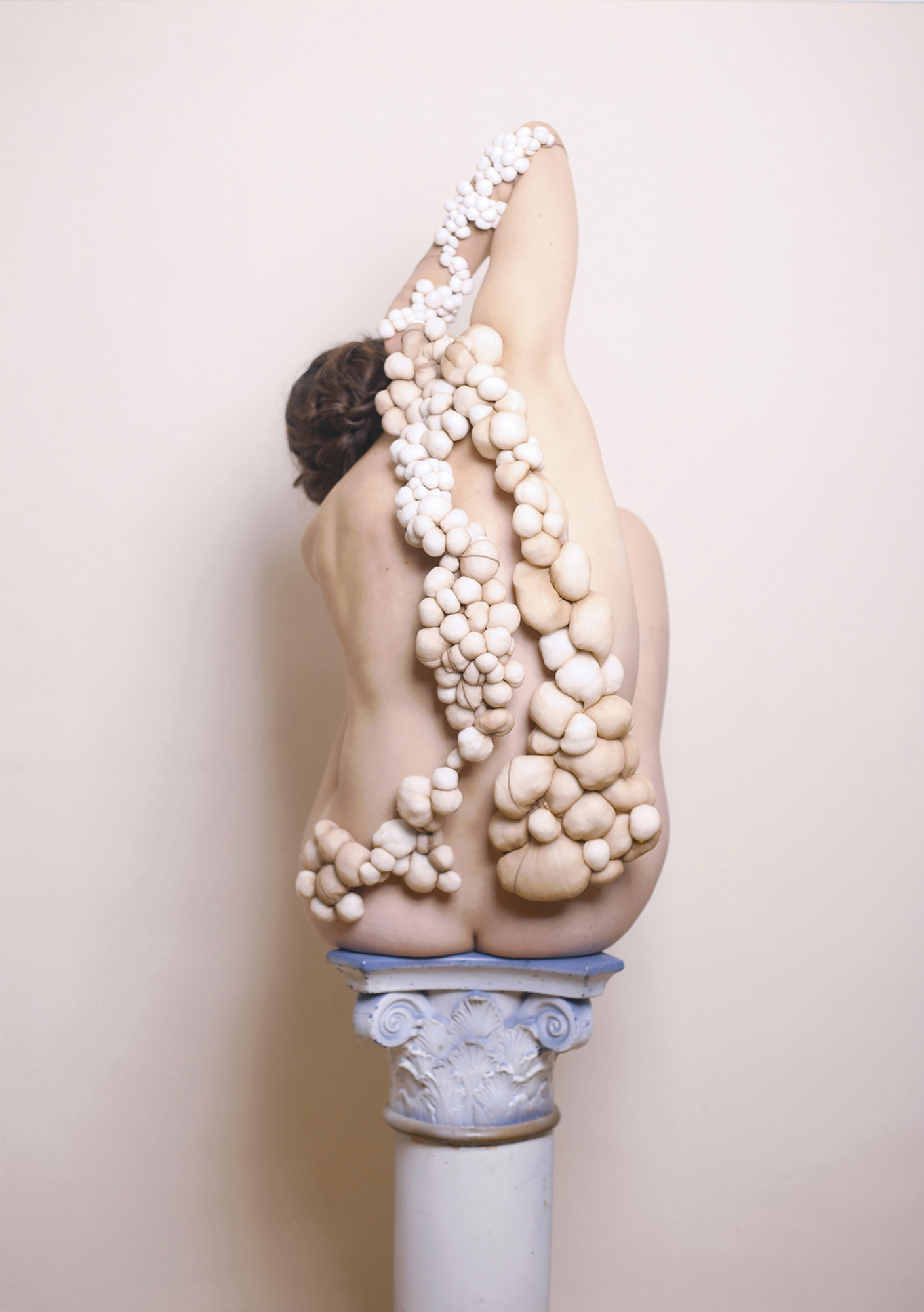 A naked figure is covered in round material objects.