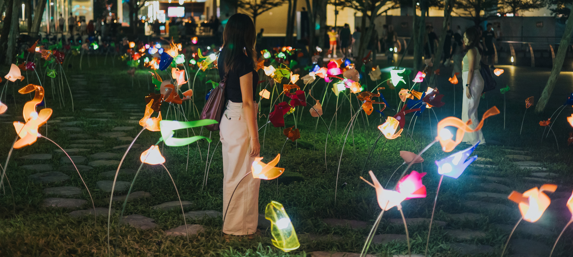A woman standing in a green space filled with flower-shaped lights. 