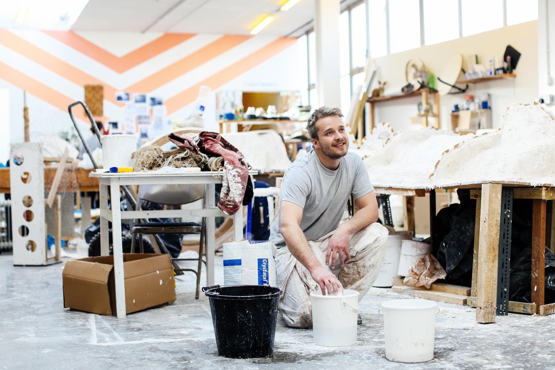 A person smiling whilst working with plaster in the studio