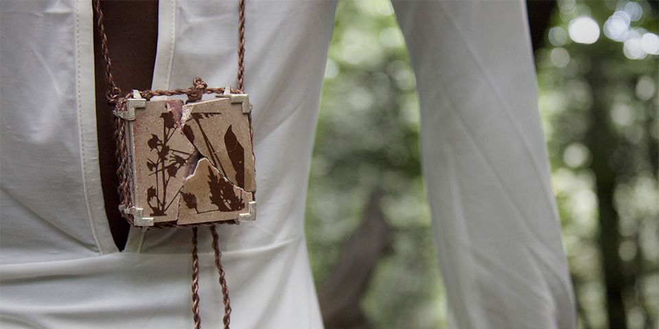 A small cracked ceramic box on a piece of rope which is worn around a person's neck