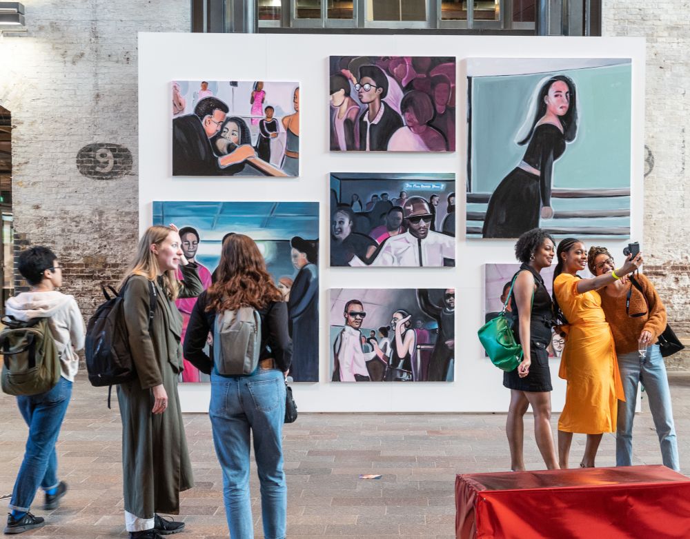 People gathering around a wall of paintings