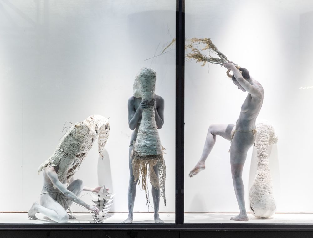 Three figures painted white making shapes in a window