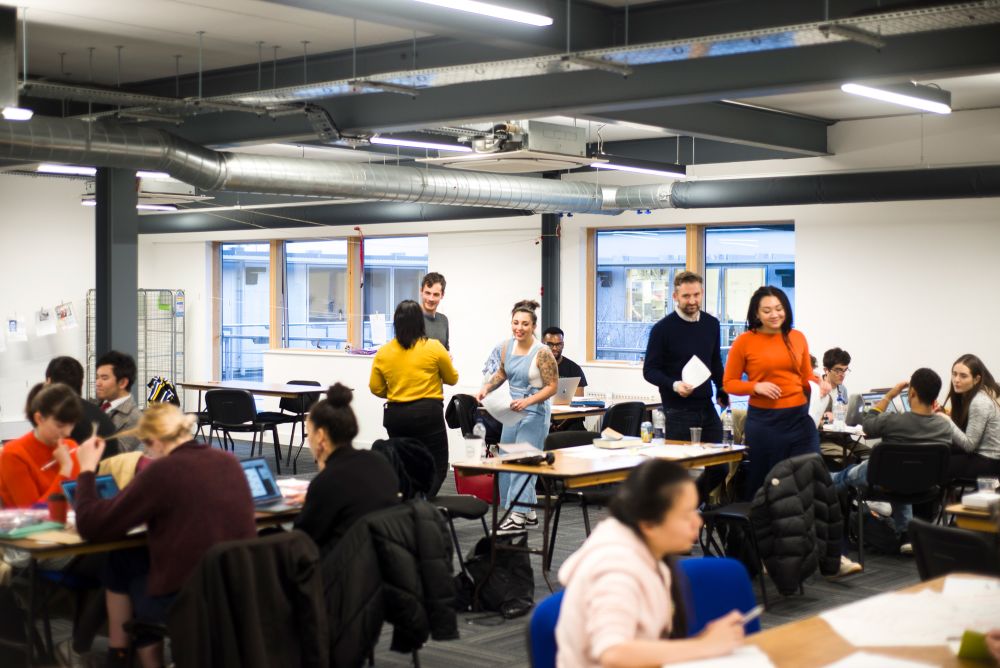 Students and industry volunteers working at desks in the studio