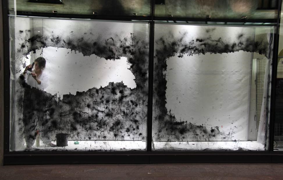 women in a a lit up window space painting glass black