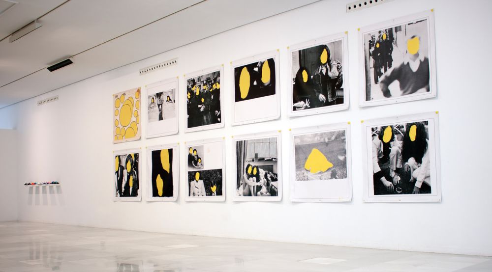 An exhibition of black and white photographs of people, with their faces replaced with yellow