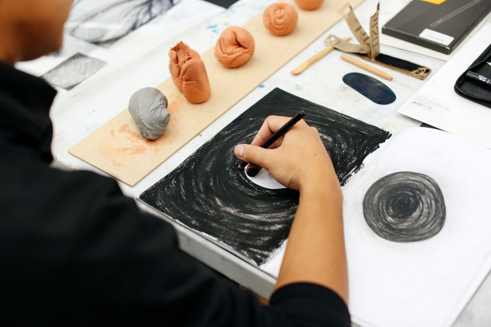 Hand using charcoal to sketch on paper