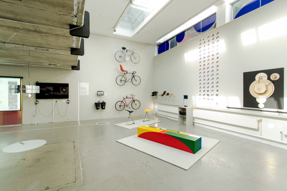 Gallery view of student work including three bikes mounted on the wall and work displayed around the walls.