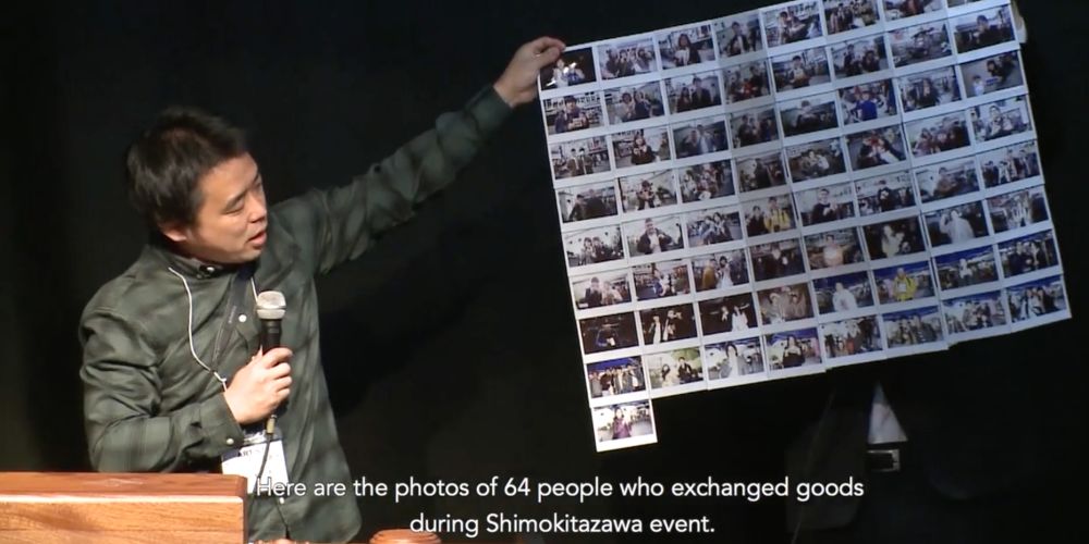 A man stood on stage, holding a microphone and holding up a poster