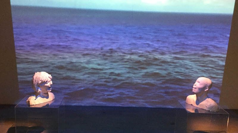 digital 3D images of heads screaming in front of a film of a rough sea