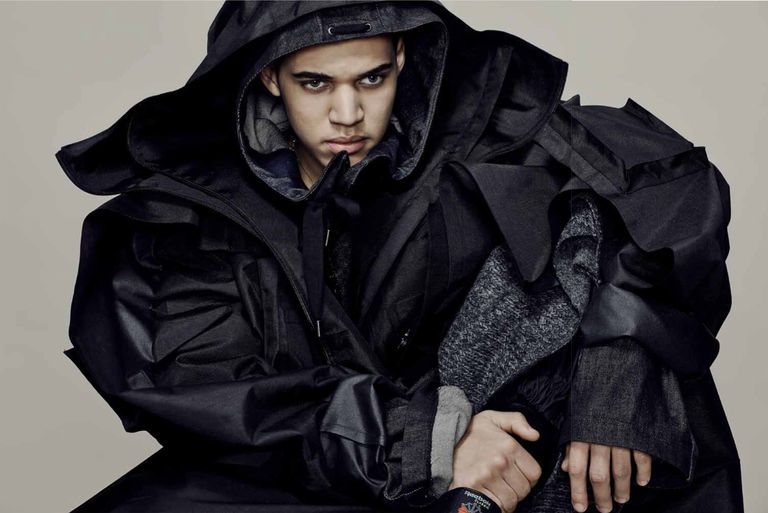 Male model in hooded coat, crouching on the ground.