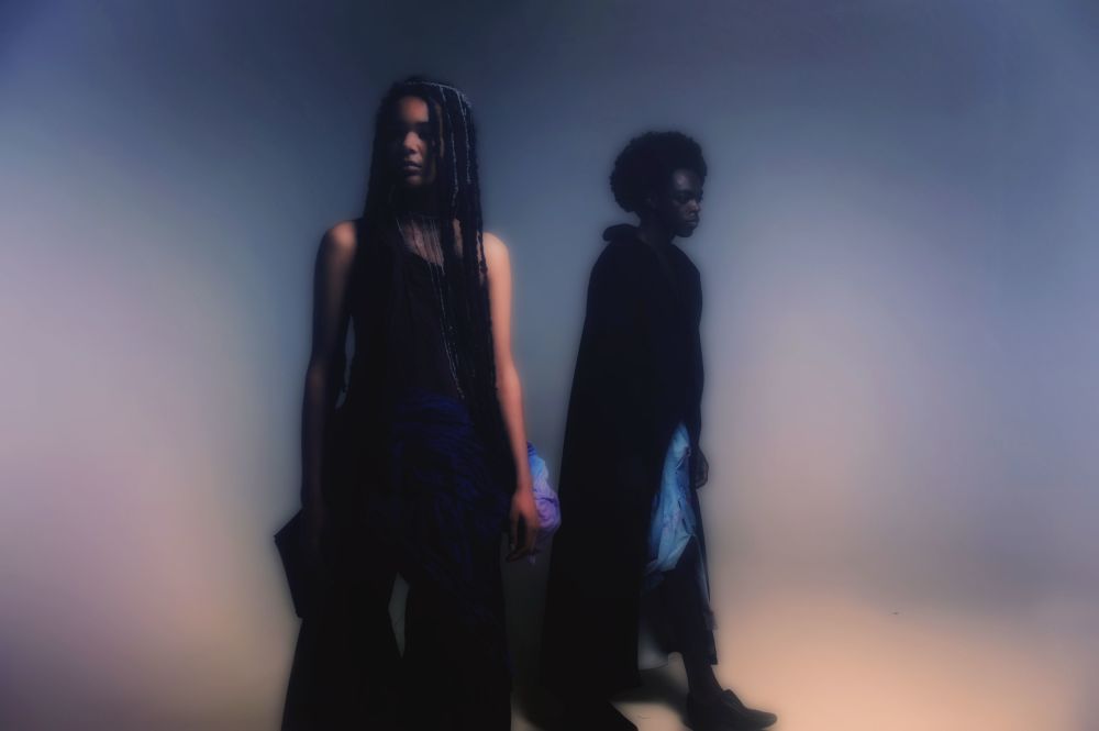 Two figures wearing blue garments in ombre background
