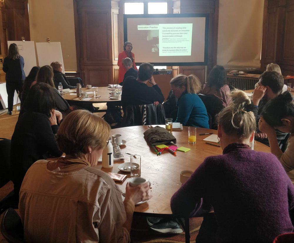 Participants sit around rouns tables and watch a presenter