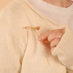 Close up photograph of someone wearing a golden brooch and holding it up against their chest between their finger and thumb