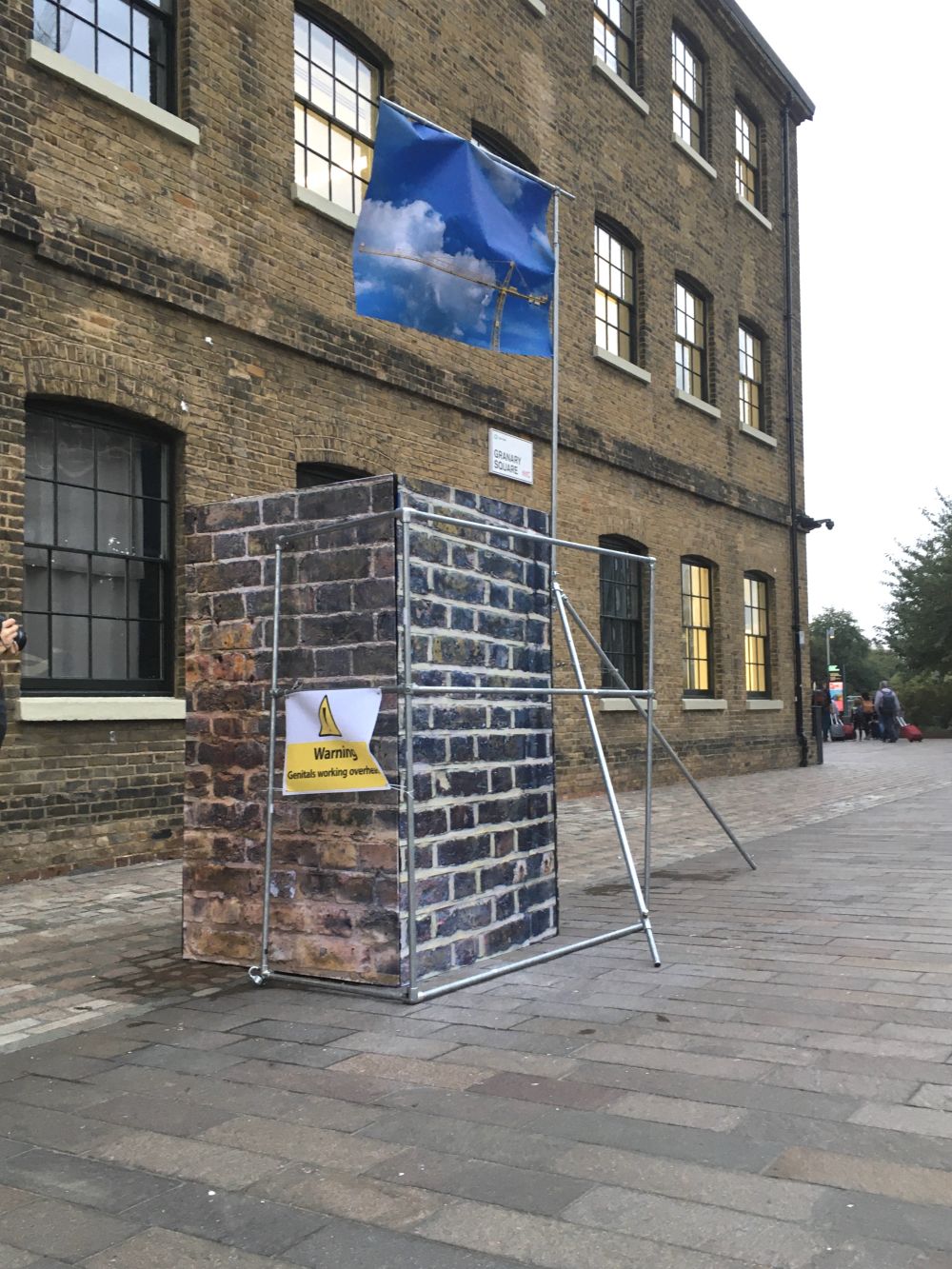 A brick front structure with scaffolding and a flag with a picture of a crane against blue sky