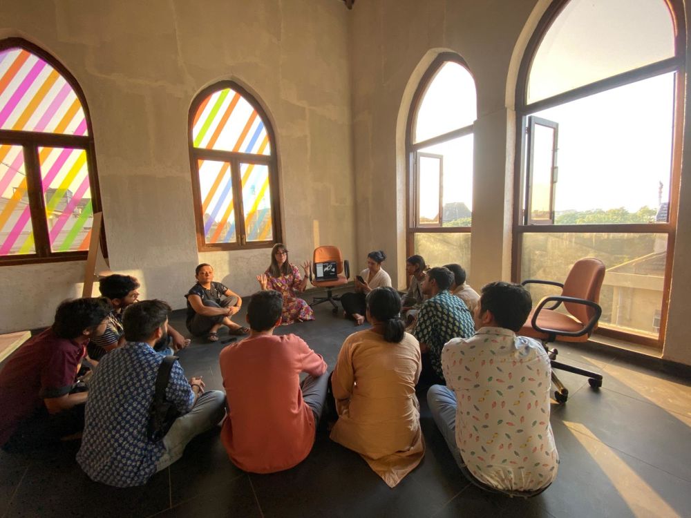 Earlier this year Charlie curated a show in Mumbai. Here she is photographed talking to some students about the exhibition, with a piece by Liz West on the windows behind her. Image credit: Katsushi Goto