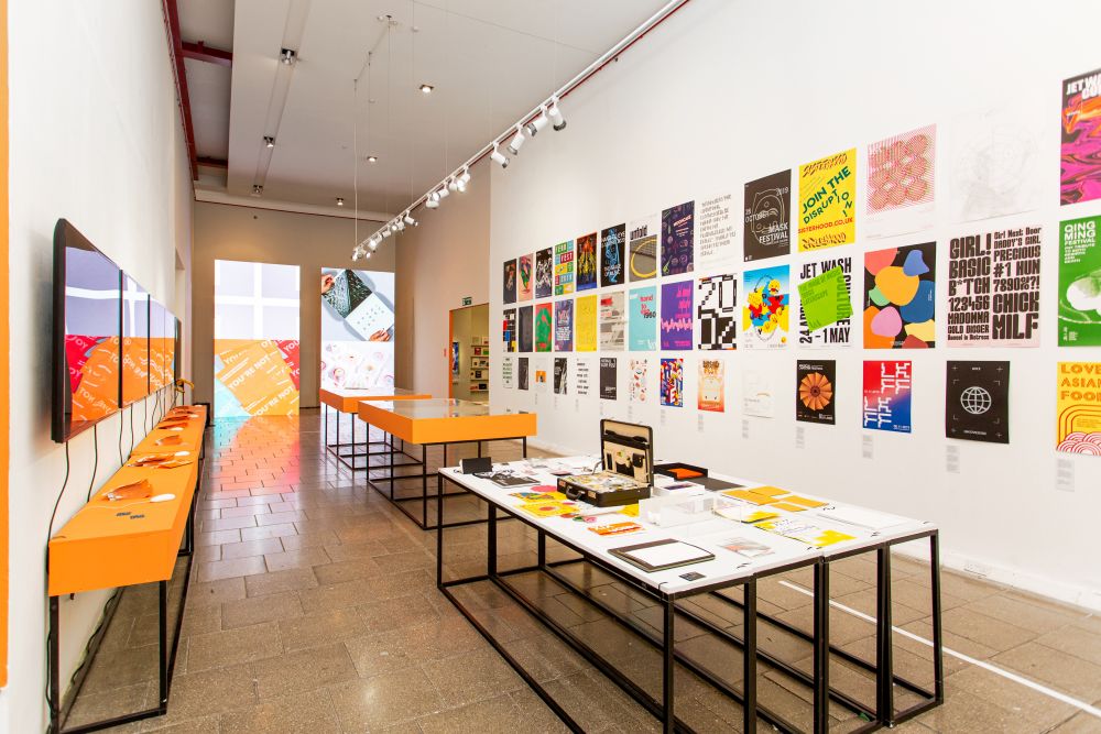 Exhibition space showing a number of posters on the wall and display tables.