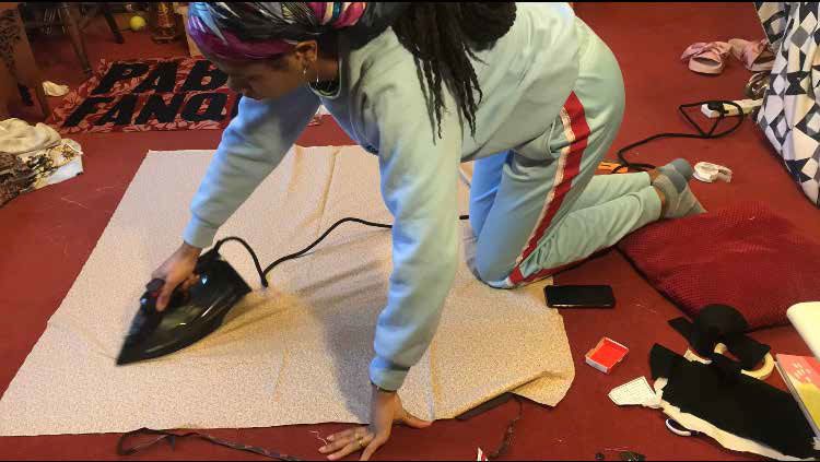Woman sitting on floor ironing piece of fabric