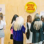 Photograph of a group of people looking at artwork on display, taken from behind them