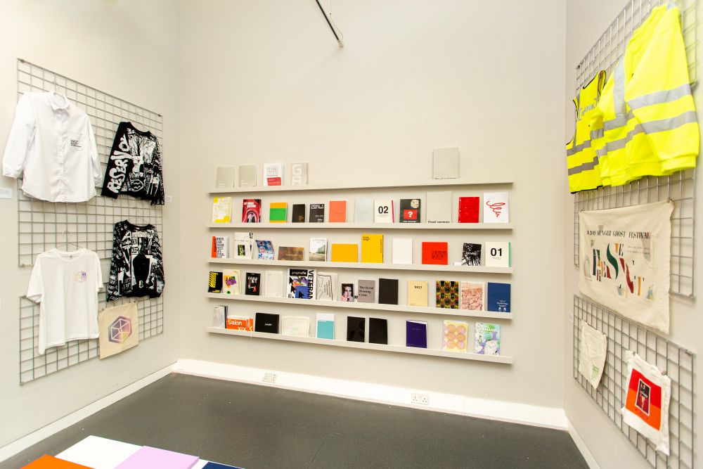 Gallery view of student work including books and magazine on shelves and clothing designs.