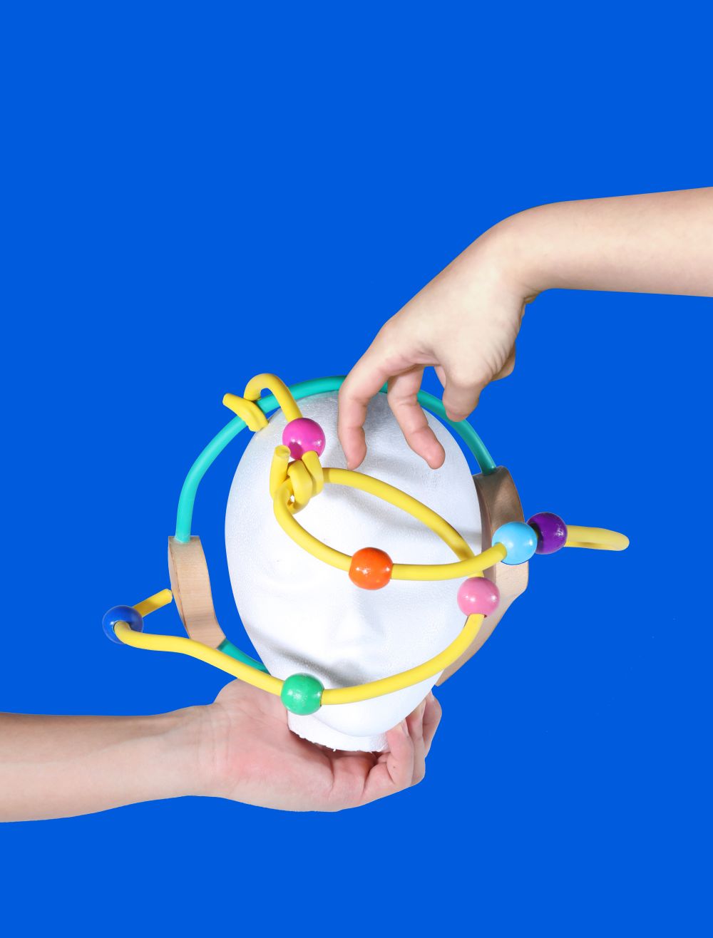 handheld artefact with colourful wires and beads, against a blue background