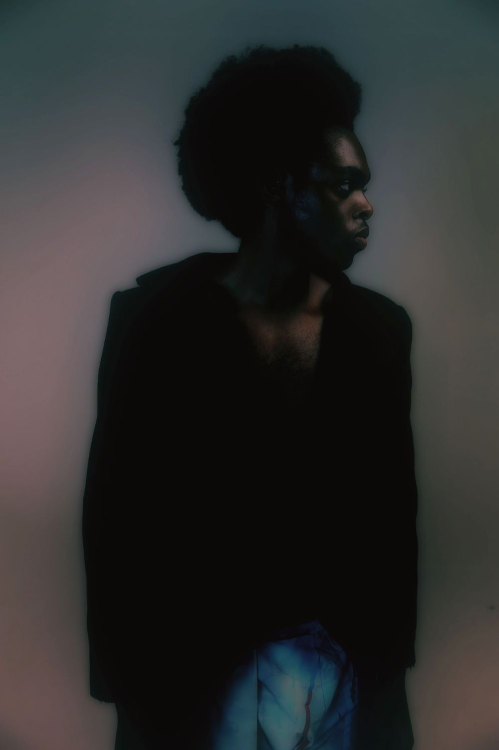 Figure wearing dark garments, set against a vignetted background