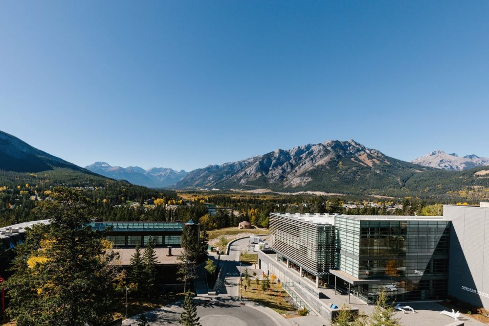 Landscape image of mountains in canada with people sat on grass verge 