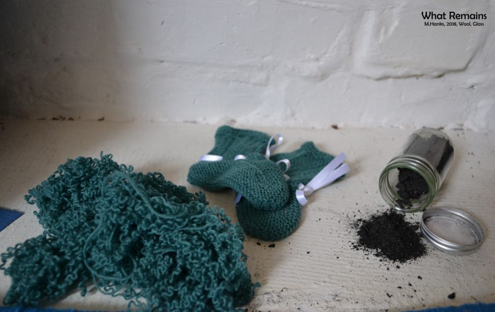 a picture on green knitted baby slippers with a bottle of dark poweder spilled next to them