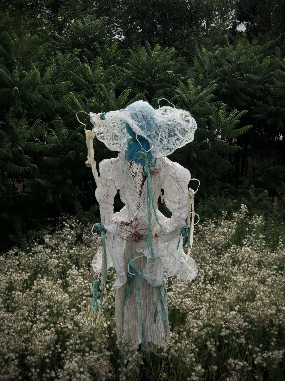 Handcrafted mannequin in meadow dressed in variety of fabrics.